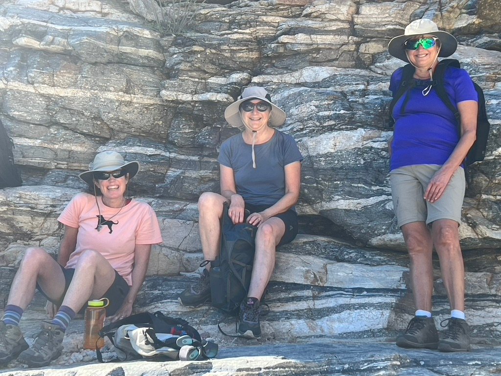 Three people sitting and standing on a rock